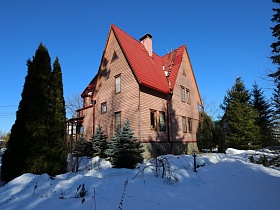 общий вид двухэтажной загородной дачи с красной крышей  в сказочном стиле на участке под снегом