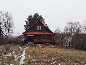 небольшой уютный деревянный домик с окном под треугольной крышей, навесом над крыльцом у входной двери на участке в деревне в зимнее время