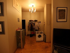 напольная вешалка с одеждой у входной двери в прихожую с картинами и домофоном на стенах разноплановой простой квартиры