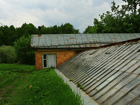 стеклянная треугольная крыша просторной теплицы у кирпичного дома в яблоневом цветущем саду - ЛГ