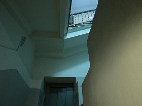 винтовая лестница стильного подъезда 12 после ремонта жилого дома эпохи СССР с серыми панелями белых стен и белым потолком