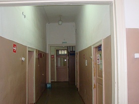 светлый коридор с закрытыми дверьми в санкомнаты с указателями на стенах старой деревянной больницы