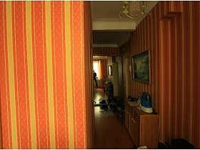 коричневая тумбочка у стены с большой картиной, белым домофоном на стене прихожей с большим шкафом-купе с зеркальными дверцами и обувью у входной двери