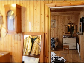 вид на белый комод с зеркалом на стене гостиной из открытой двери прихожей деревянной дачи
