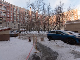  огнизкий металлический забор вокруг площадки с высокими деревьями на придомовой территории, припаркованные машины у подъездов сталинских домов в зимнее время