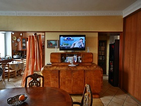 большой телевизор и картина на стене над необычной деревянной старинной мебелью между дверными проемами гостиной квартиры эпохи СССР