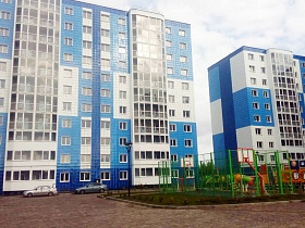 красивые сине-бело-голубые многоэтажные жилые дома новостройки с застекленными лоджиями со спортивной площадкой, детским игровым комплексом на придомовой территории