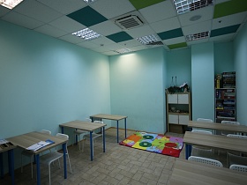 два деревянных шкафчика с методической литературой, учебным пособием на полках в нише учебного класса с голубыми стенами, разноцветным ковриком на полу детского центра
