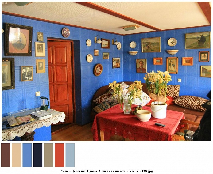 цветы в вазе, горшочке на столе с красной скатертью, угловой мягкий диван с подушками у голубой стены, украшенной многочисленными картинами, фотографиями, декоративными тарелками в одной из комнат сельского дома