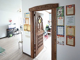 многочисленные грамоты и дипломы на стене у межкомнатной резной деревянной двери с якорем в простой семейной квартире