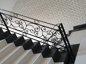 вензеля на черных перилах лестницы с двухцветными ступенями в стильном современном подъезде