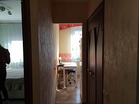 стулья и белый стол на полу с квадратной плиткой кухни из открытого дверного проема прихожей с бежевыми стенами двухкомнатной квартиры
