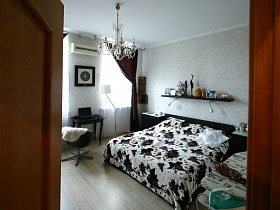 большая кровать с белым пятнистым покрывалом, с прикроватными тумбочками в красивой спальне трехкомнатной квартиры