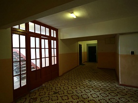 общий вид чистого просторного холла сталинского дома с высокими деревянными дверьми под стеклом на лестничную площадку между этажами