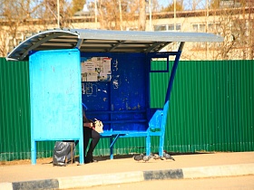 крытый синий павильон со скамейкой на автобусной остановке в Сычево у зеленного высокого забора для съемок кино