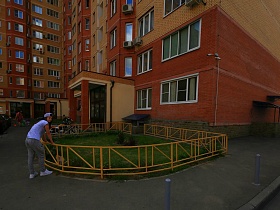 полисадник с желтой оградой у подъезда современного двухцветного дома