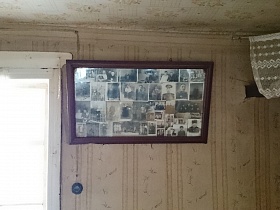 старинные военные фотографии в рамке под стеклом у окна на стене с полосатыми обоями комнаты в доме заброшенной деревни