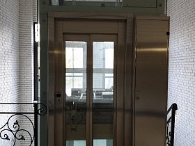 черные фигурные кованные перила у входной стеклянной двери в лифтовую кабину подъезда современного жилого дома