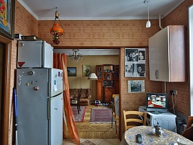 белый холодильник в углу, коллаж из фотографий на стене у дверного проема с ораньжевой шторой кухни советской трехкомнатной квартиры