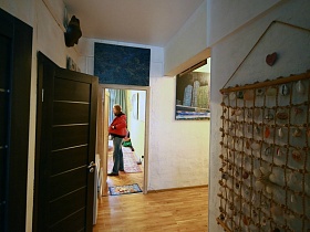 вид из кухни на декоративное пано на стене коридора, красочные картины на светлых стенах прихожей и над открытой дверью спальной комнаты лофт квартиры художника