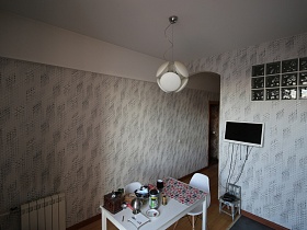 стильная люстра над белым обеденным столом на белом потолке уютной современной кухни с тесненными серыми обоями на стене в квартире советского и современного времени