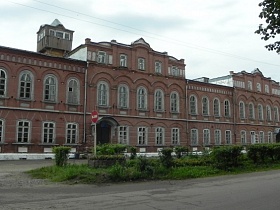 длинная трехэтажная кирпичная старинная школа с многочисленными арочными окнами на открытой площадке вдоль дороги