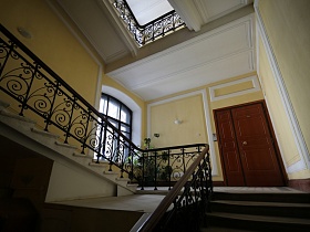 двери жилой квартиры на лестничной площадке с большим окном, лестницей с резными перилами между этажами в подъезде дома советского времени