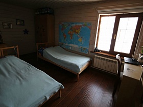 две деревянные кровати, большая карта мира на стене и письменный стол у окна спальни в современном деревянном просторном доме