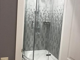 душевая кабинка с прозрачными стеклянными дверцами у стены с серой плиткой ванной комнаты однокомнатной квартиры маленького размера в сером цвете