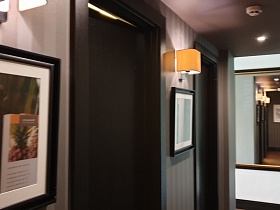 картины и зеркало в коричневых рамках, бра на светлых полосатых стенах длинного коридора ресторана Академия