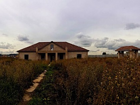 недостроенное дом и различные постройки на неухоженном участке в коттеджном поселке на берегу реки