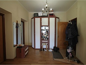 маленький телевизор, различные коробки на коричневом шкафу с белыми дверцами и обувь под маленьким стульчиком у входной двери в простую комнату на Садовом