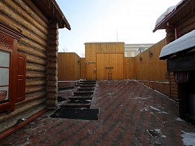 просторный двор, выложенный квадратной брусчаткой за деревянным забором с уличными фонарями на стенах