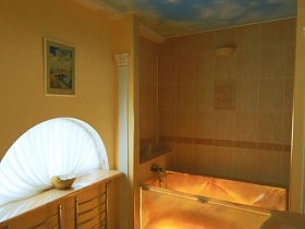 оригинальная подсветка ванны у стены с бежевой плиткой и отражением голубого неба с облаками на потолке ванной комнаты дизайнерской дачи в сосновом лесу