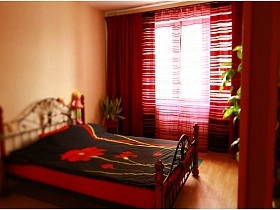 красный матрас и деревянные ножки большой кровати с красными маками на одеяле в восточной спальне простой квартиры для съемок кино