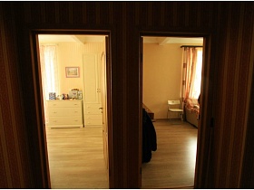 открытые коричневые деревянные двери в смежные комнаты - светлую спальню во французском стиле и гостиную стильной двухкомнатной квартиры