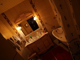 красные дорожки у белой ванны на ножках и тумбы с раковиной, табурет, полотенца и большое зеркало со светильниками на стене ванной комнаты, выложенной плиткой в загородном доме с башней