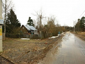 мокрая асфальтированная проезжая дорога мимо двора деревянной избы