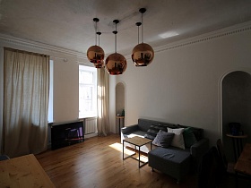 черный плоский телевизор на деревянном полу белой гостиной между окнами с кремовыми шторами современной скандинавской квартиры