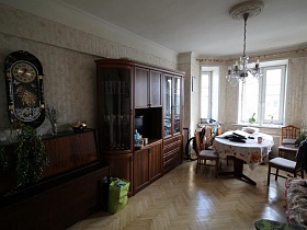 большие часы на стене над пианино, люстра, стилизованная  под свечи на белом потолке в гостиной квартиры сталинки