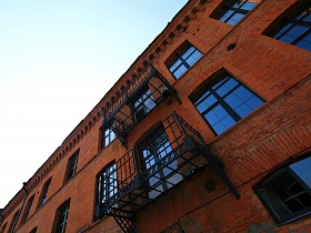 стеклянный пол открытых балконов с черным металлическим ограждением на стенах кирпичного здания