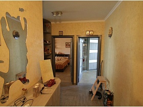 иконы над открытыми дверьми в гостиную и спальню из прихожей с зеркалом в виде кота над полукруглым комодом в двухкомнатной квартире новостроя