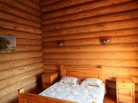 небольшой коврики на полу и прикроватные тумбочки у деревянной кровати с покрывалом и подушками в комнате отдыха деревянного домика с баней