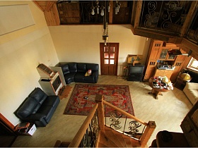 общий вид сверху гостиной с цветным ковром посередине, черными кожаными диванами у стены, светлым мягким диваном и шкафом у окна