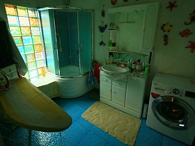 гладильнвя доска с утюгом, душевая кабина, полочки на стене над белой круглой  раковиной в столе, стиральная машина в ванной комнате современной классической семейной дачи