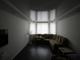 телевизор, картина на белых стенах светлой комнаты с натяжным потолком и мягкой бежевой мебелью у эркерного окна двухкомнатной квартиры в Котельниках