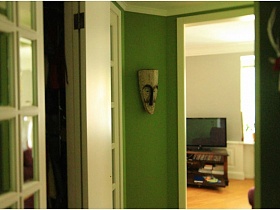 телевизор на тумбе через открытую дверь прихожей с зелеными стенами в однокомнатной квартире жилого дома