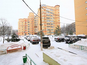 расчищенная от снега придомовая территория кирпичных жилых многоэтажек за невысоким цветным металлическим забором