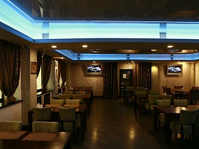 плоские телевизоры на бежевых стенах по обе стороны от входной двери,картины на кирпичных колонах просторного зала с подвесным потолком хорошего ресторана на Юге Москвы