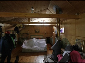 светлый диван, накрытый белой простынью у кровати в спальной зоне деревянного домика на дачном участке